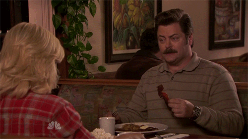 A scene from NBC’s Parks and Recreation show where character Ron Swanson is eating bacon at a diner with character Leslie Knope.